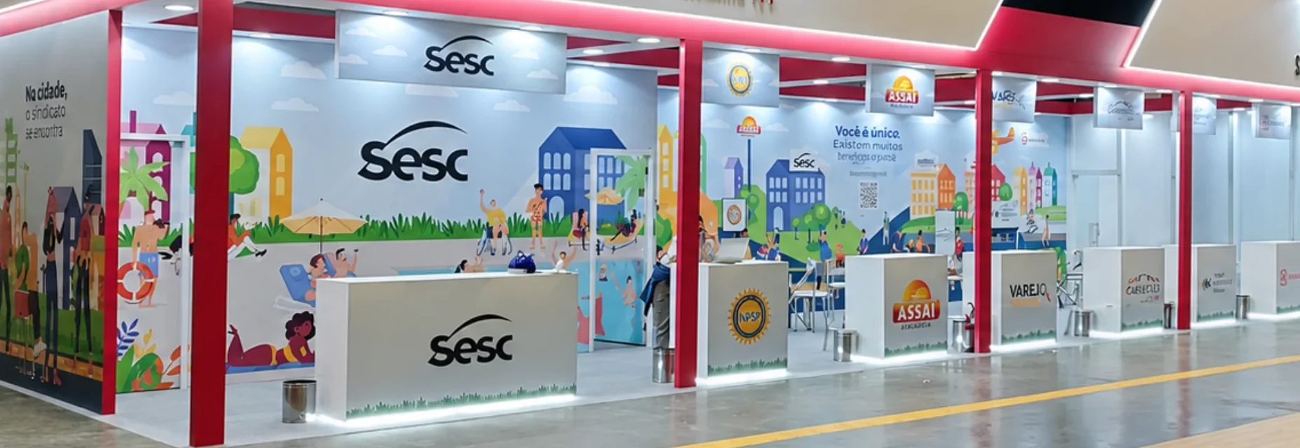 A extensão do estande vista de frente: a parede ilustrada da cidade corre atrás de uma sequência de balcões brancos — Sesc, Nurap, Assaí Atacadista, Varejo Contrata, Grupo Carrefour Brasil e Mackenzie — sob a estrutura vermelha.