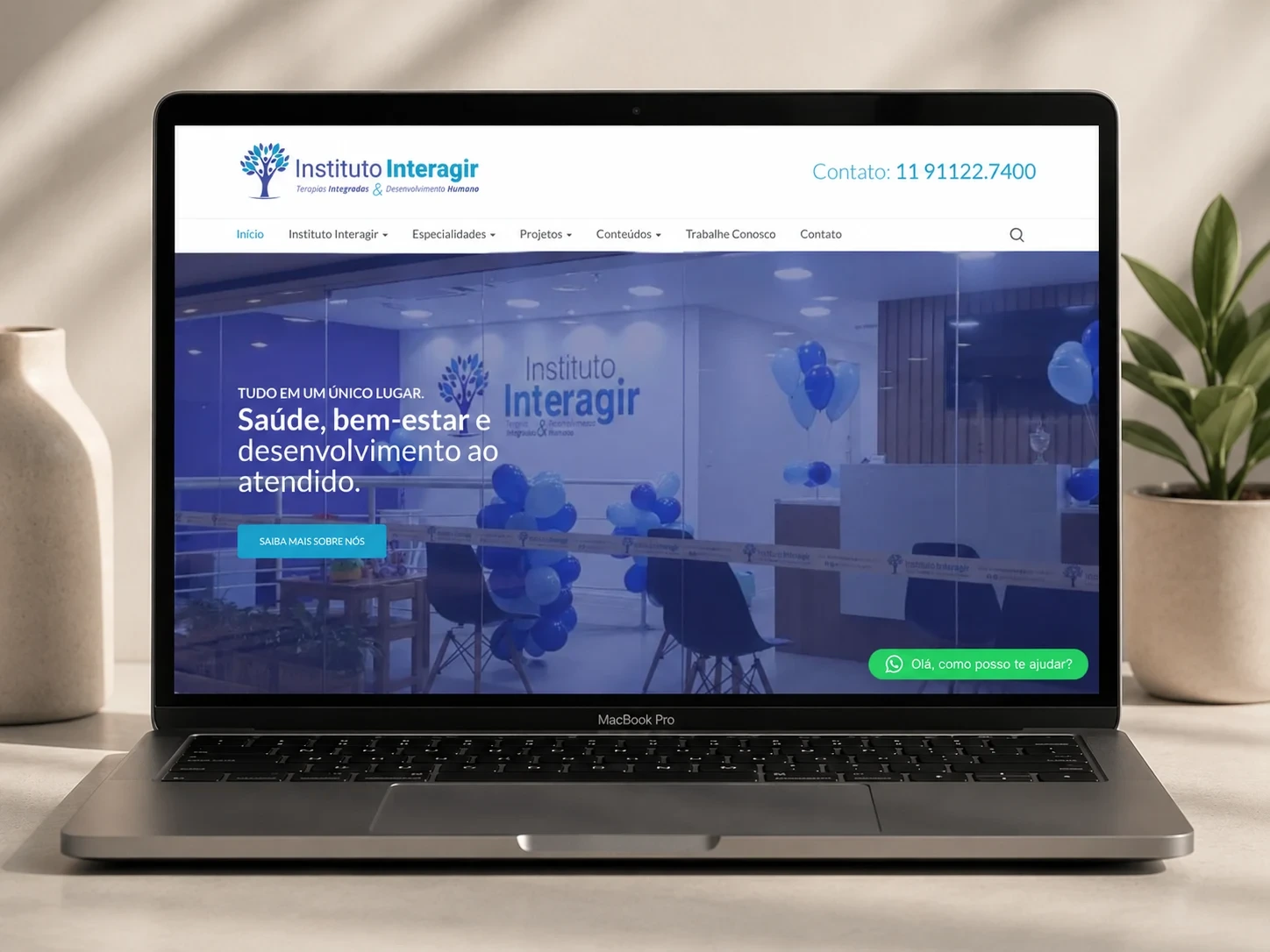O site do Instituto Interagir aberto em um notebook, com a marca no topo, o menu de especialidades e a chamada “Saúde, bem-estar e desenvolvimento ao atendido”.